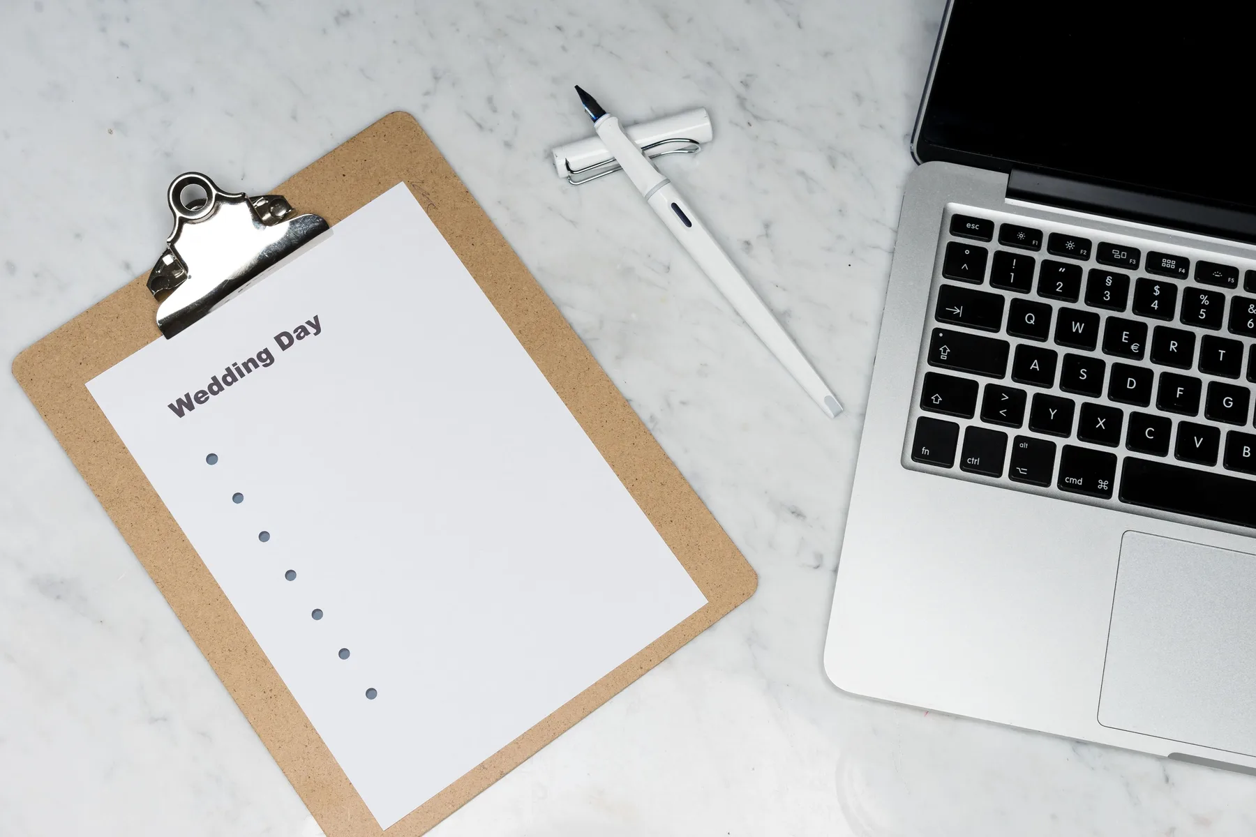 Plan de organizare a nunții pe un clipboard, lângă un laptop și un stilou